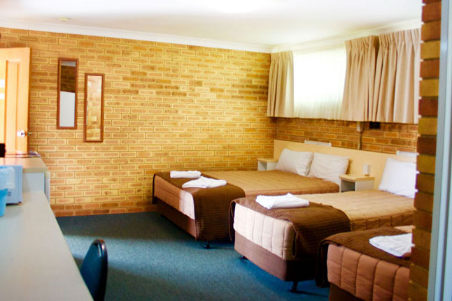 A room with brown brick walls and has two brown single beds and one brown queen bed